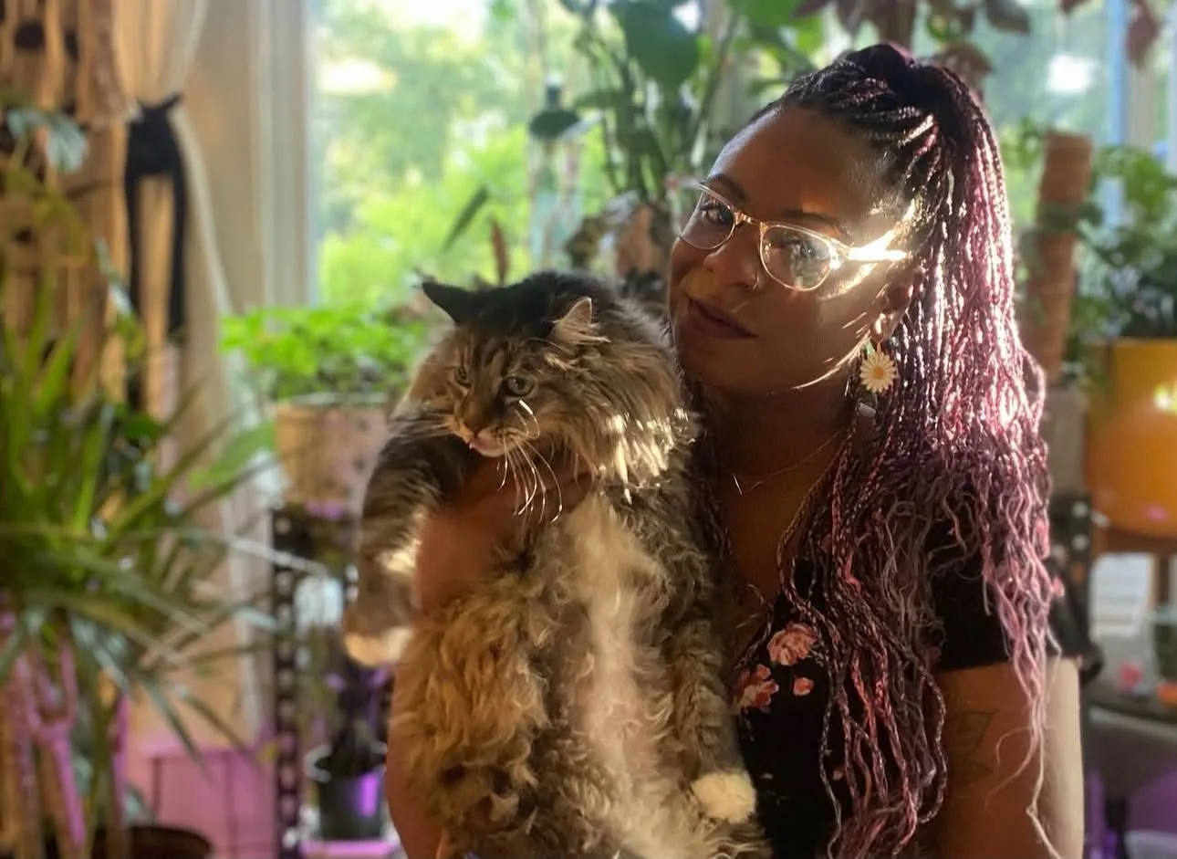 Paula holding her cat in a sunlit, plant-filled room